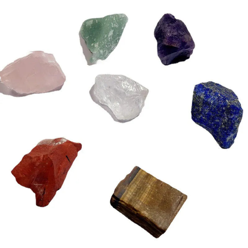 Seven natural white crystal rough stones in rainbow chakra colours on a flat surface