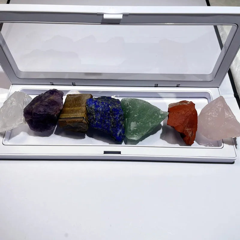 Seven natural white crystal rough stones in rainbow chakra colours on a flat surface