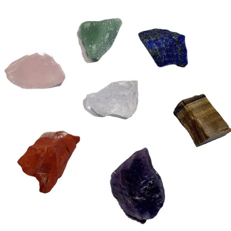Seven natural white crystal rough stones in rainbow chakra colours on a flat surface