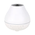 White round Bluetooth humidifier and aroma diffuser with night light on a wooden table, emitting mist.