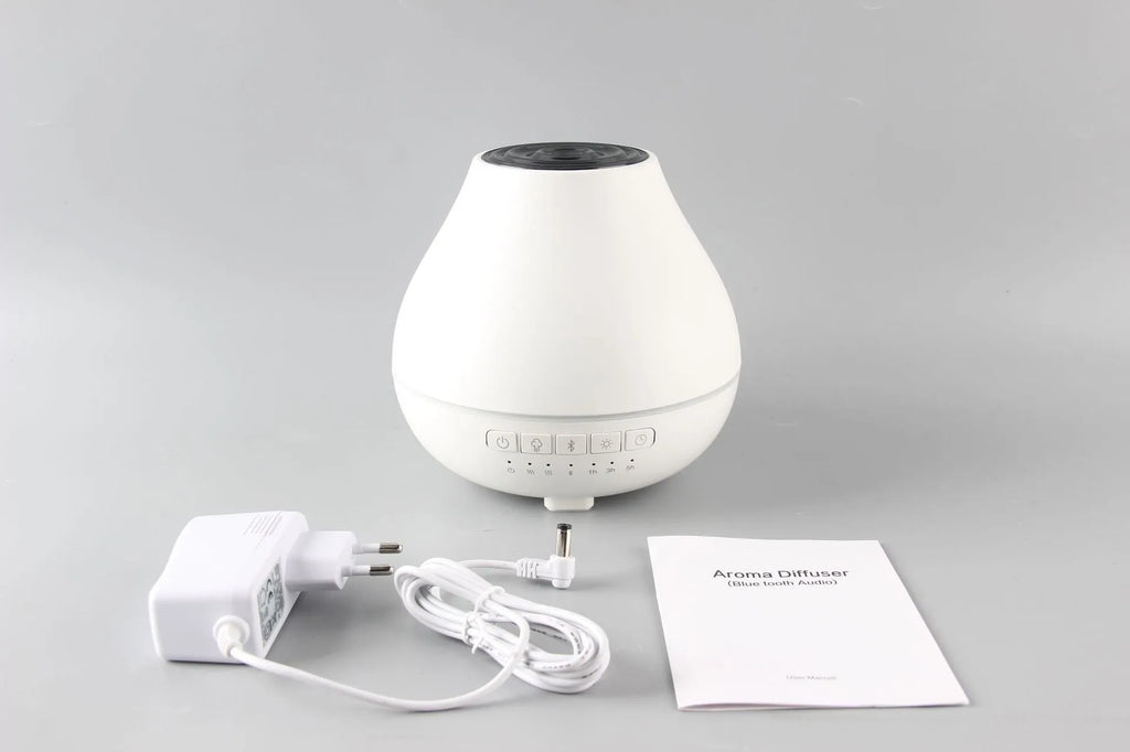 White round Bluetooth humidifier and aroma diffuser with night light on a wooden table, emitting mist.