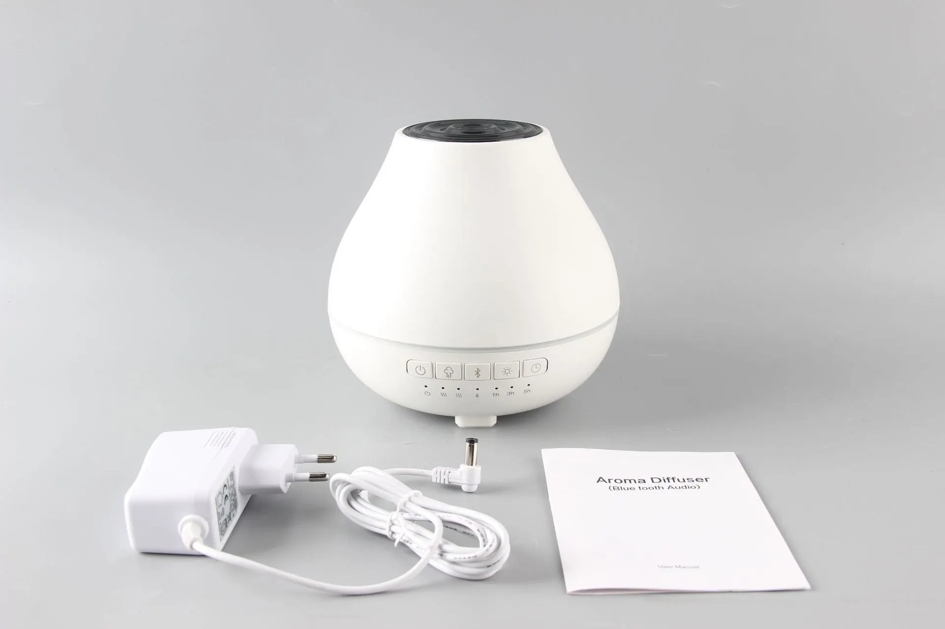 White round Bluetooth humidifier and aroma diffuser with night light on a wooden table, emitting mist.