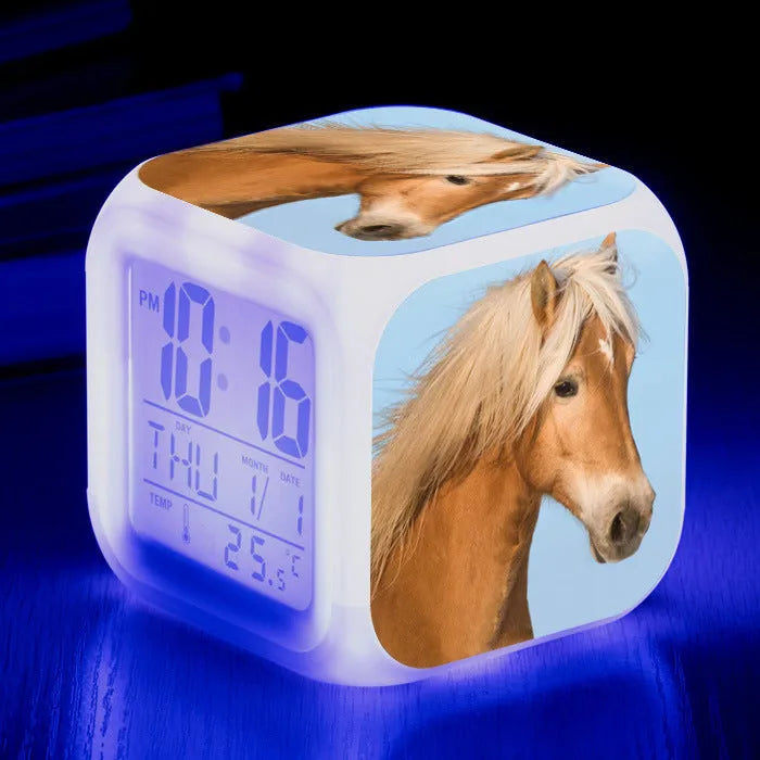 Square cartoon-style colour-changing LED alarm clock showing time and temperature on a desk.