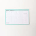 Domikee paper desk organiser pad open showing weekly and monthly planning templates with pink and green cover.