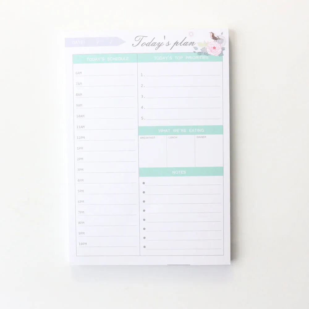 Domikee paper desk organiser pad open showing weekly and monthly planning templates with pink and green cover.
