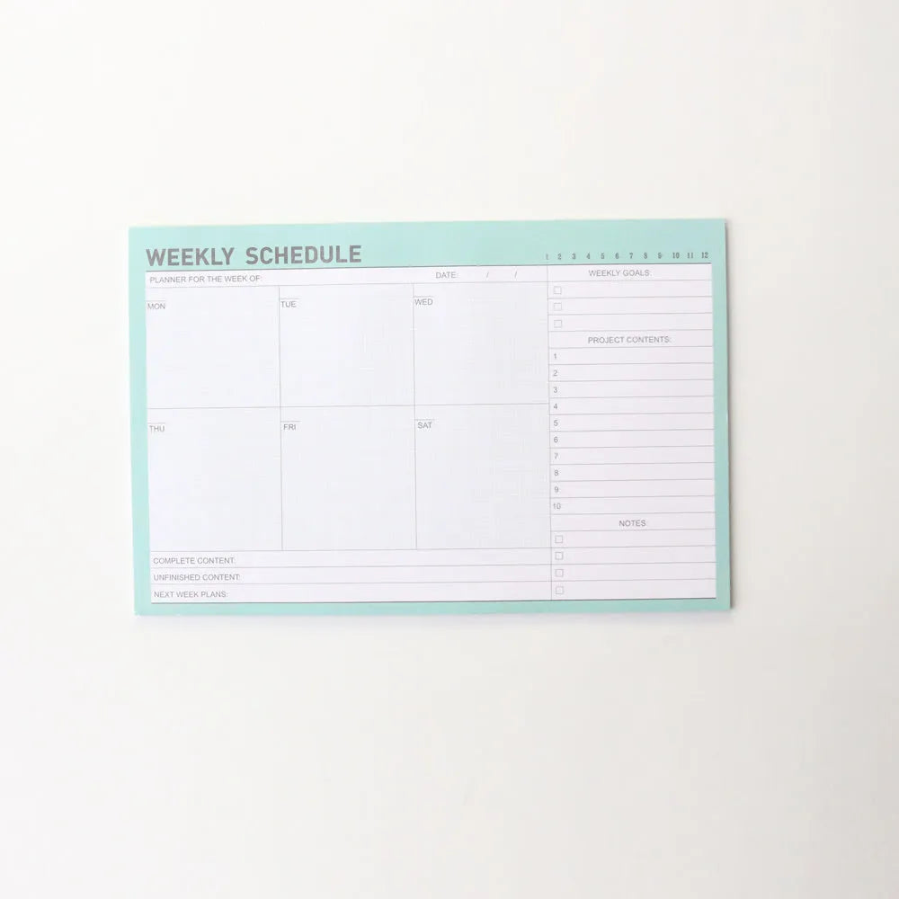 Domikee paper desk organiser pad open showing weekly and monthly planning templates with pink and green cover.