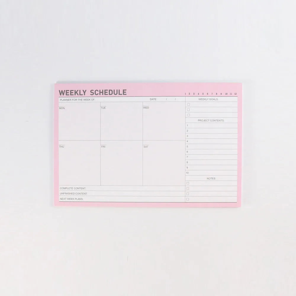 Domikee paper desk organiser pad open showing weekly and monthly planning templates with pink and green cover.