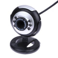 A black computer webcam with a ring of six LED lights around the lens, shown on a desktop.