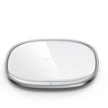 Black square 15W wireless charging pad with glass top on a wooden desk next to a smartphone.