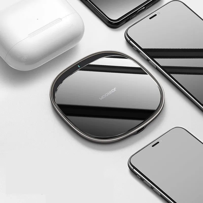 Black square 15W wireless charging pad with glass top on a wooden desk next to a smartphone.