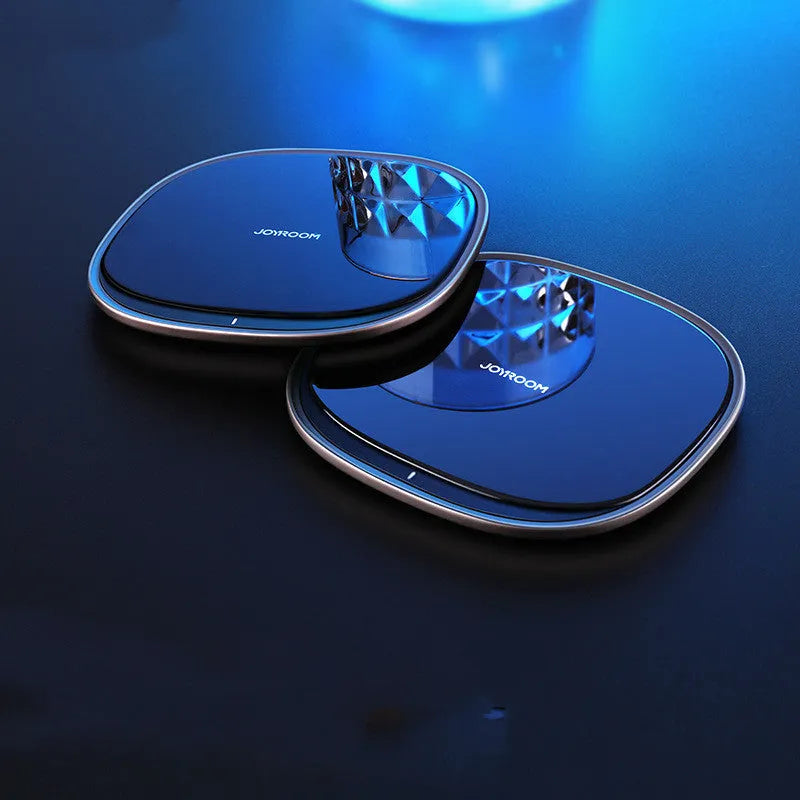 Black square 15W wireless charging pad with glass top on a wooden desk next to a smartphone.