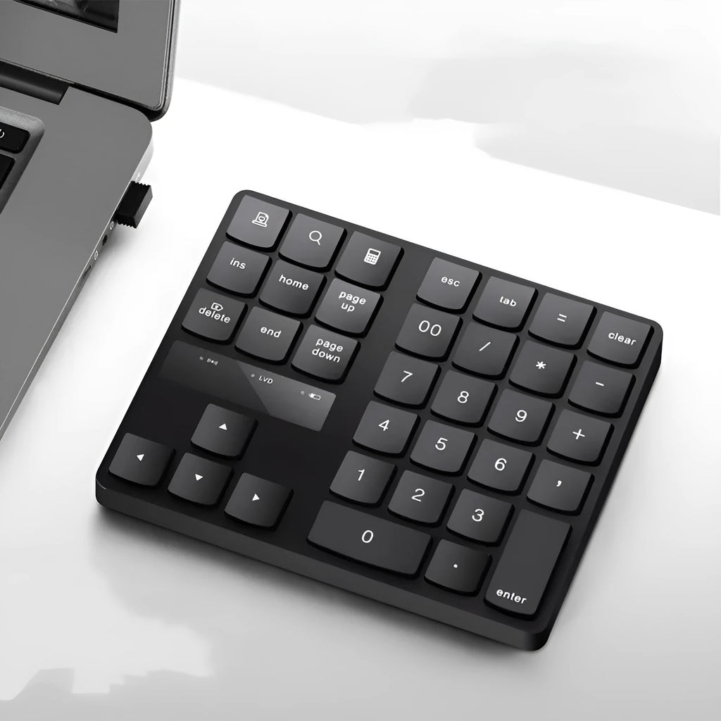 Black wireless numeric keyboard with 35 keys on a desk next to a laptop
