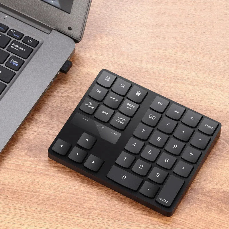 Black wireless numeric keyboard with 35 keys on a desk next to a laptop