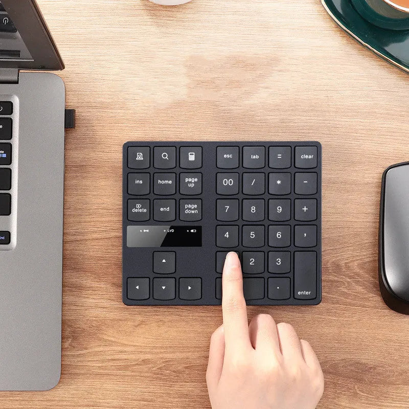 Black wireless numeric keyboard with 35 keys on a desk next to a laptop