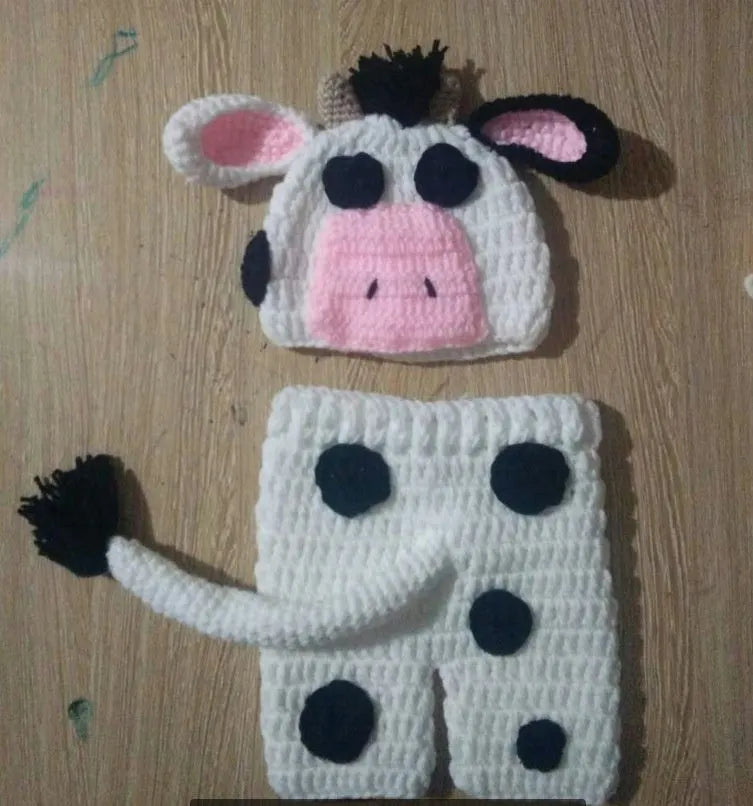 Hand-knitted white baby cow suit with hat and trousers for a newborn.