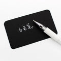 White hard pen calligraphy pen with cap closure on a dark surface showing white ink lines