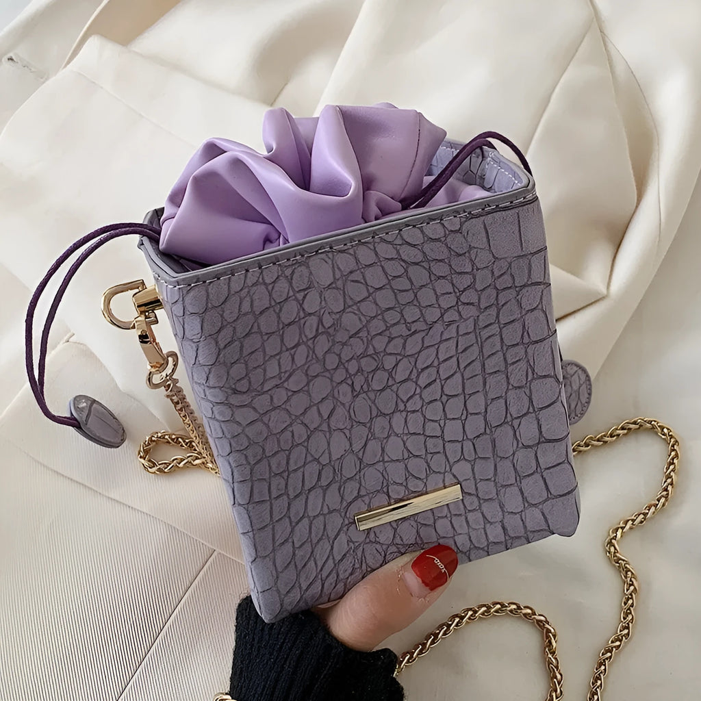 Black women's bucket-style messenger bag with a long metallic chain strap, shown with a drawstring opening.