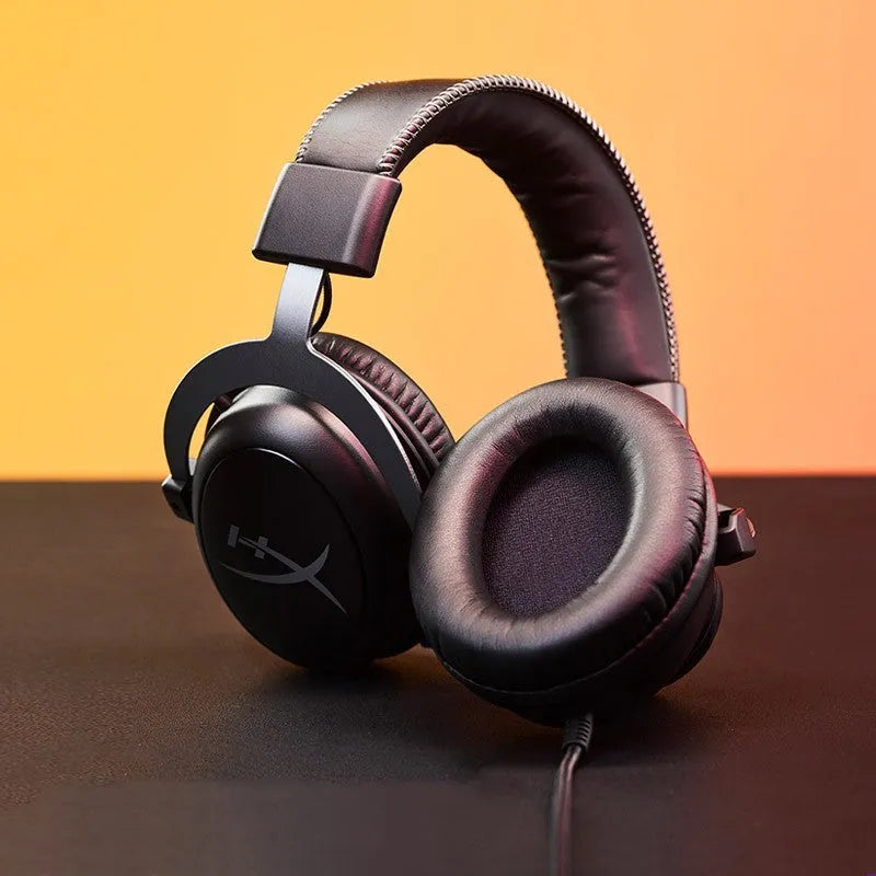 Black red wired gaming headset with detachable microphone on a desk next to a USB sound card remote control.