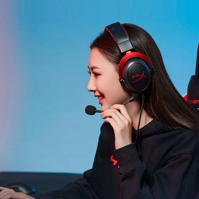 Black red wired gaming headset with detachable microphone on a desk next to a USB sound card remote control.