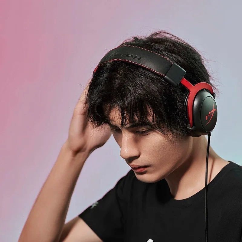Black red wired gaming headset with detachable microphone on a desk next to a USB sound card remote control.