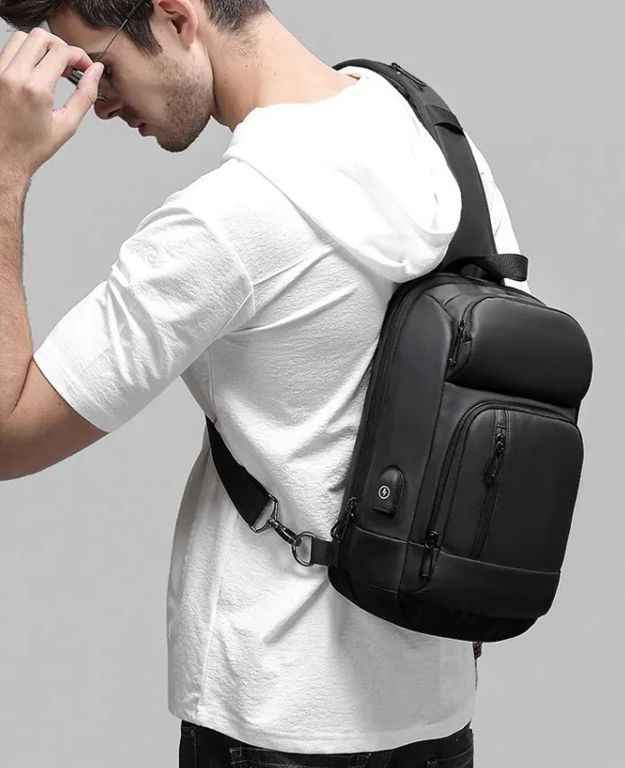 Black square PVC outdoor shoulder bag with an air cushion strap and zipper opening.