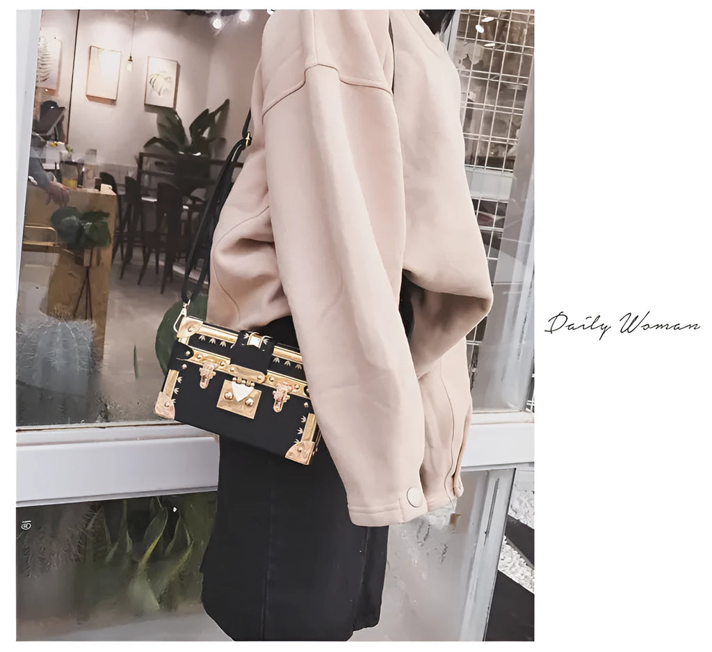 Hard-sided black women's shoulder bag with a flap closure, adjustable strap, and decorative metal rivets.