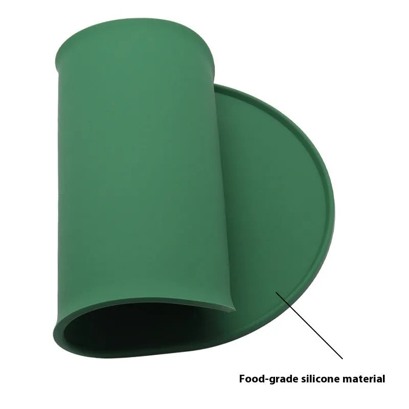 Green silicone cat feeding mat with raised edges containing dry kibble, placed on a wooden floor.
