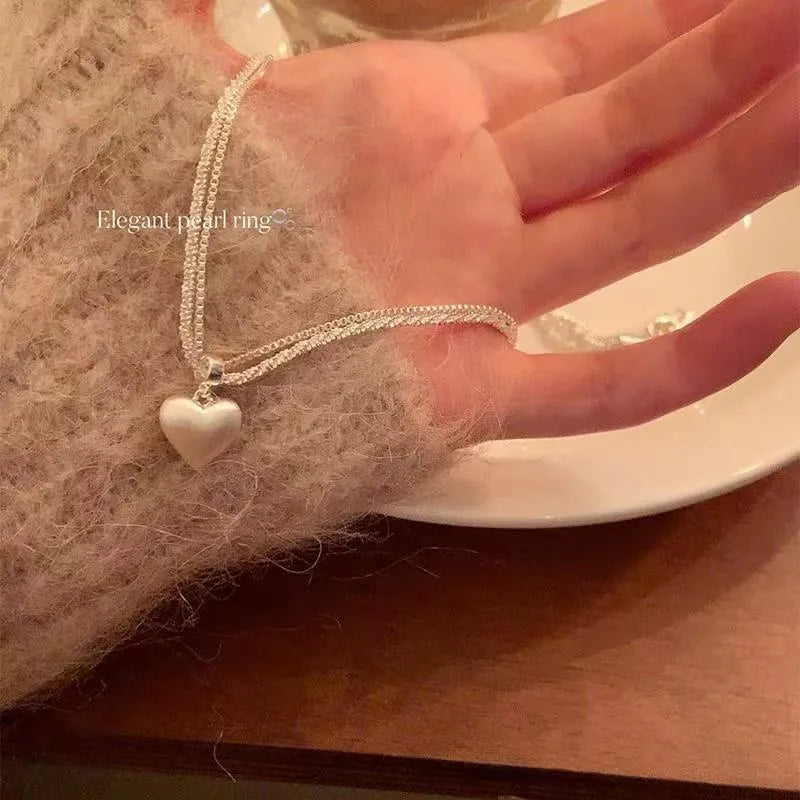 Double-layer brushed silver heart pendant necklace on a model, showing adjustable chain length.