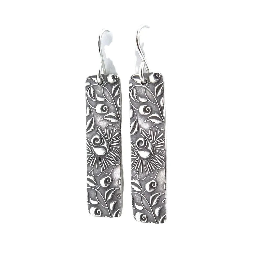 Silver geometric long strip drop earrings with carved vine pattern on a white background.