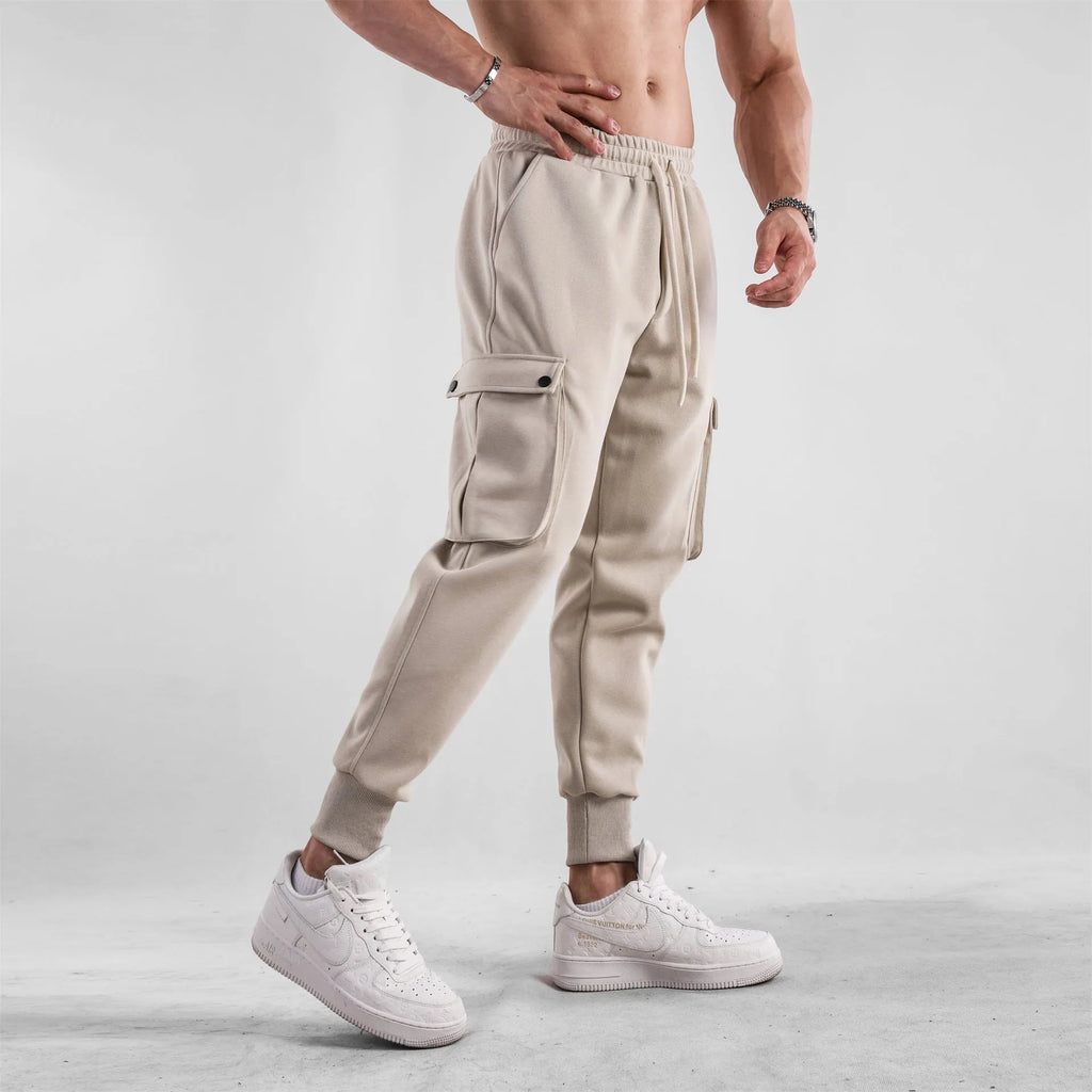 Man wearing loose-fit light grey cotton trousers with ankle ties and multiple pockets, suited for casual sports.