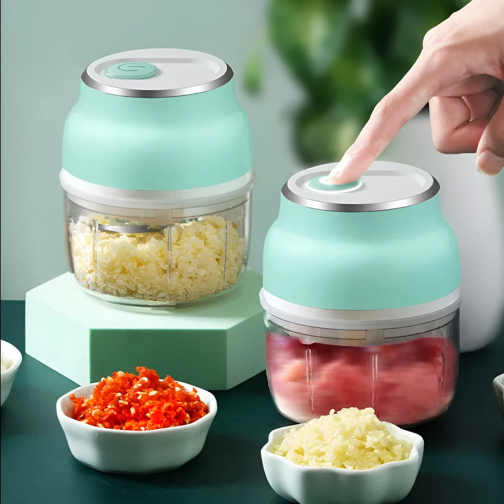 Portable electric mini garlic cutter with green body, transparent cup, and stainless steel blade on table