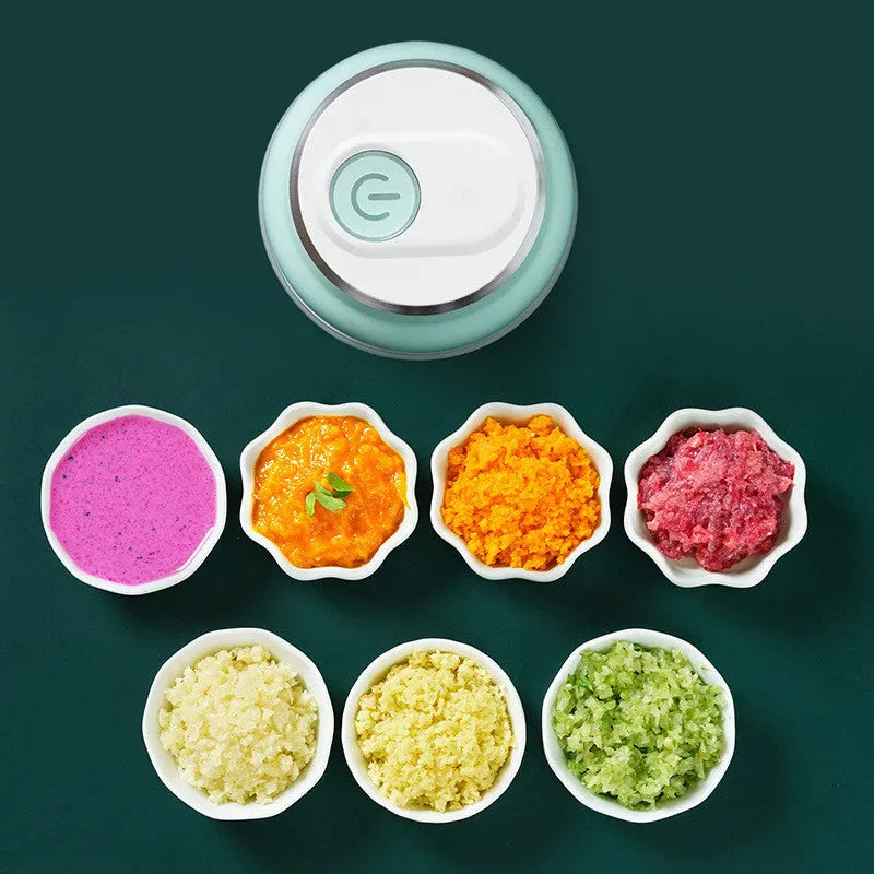 Portable electric mini garlic cutter with green body, transparent cup, and stainless steel blade on table