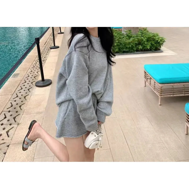 Woman wearing a loose grey knitted long-sleeve sweater and matching wide-leg shorts two-piece set.