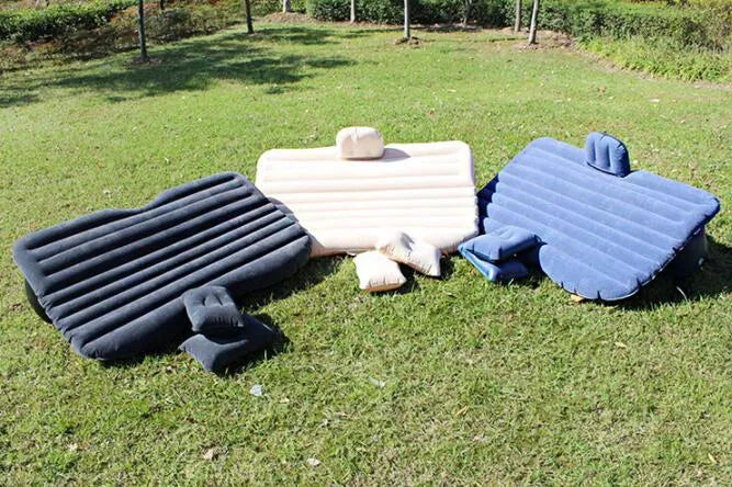 Black inflatable car bed with flocked surface and two pillows, folded next to its storage bag.