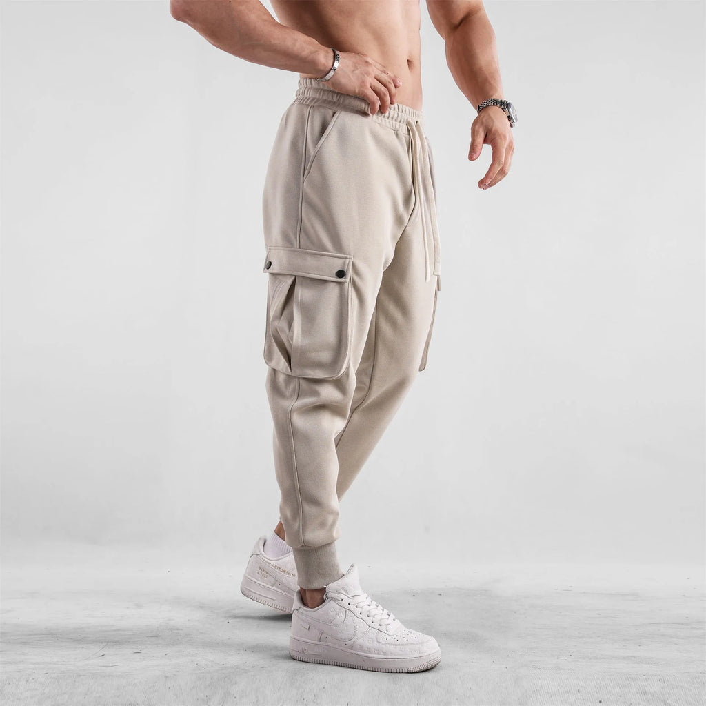 Man wearing loose-fit light grey cotton trousers with ankle ties and multiple pockets, suited for casual sports.