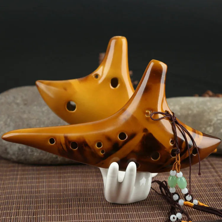 Yellow 12-hole ceramic Alto C ocarina with smoldering finish and lanyard on a surface