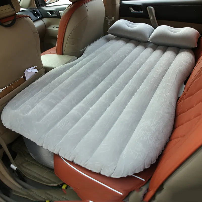 Black inflatable car bed with flocked surface and two pillows, folded next to its storage bag.