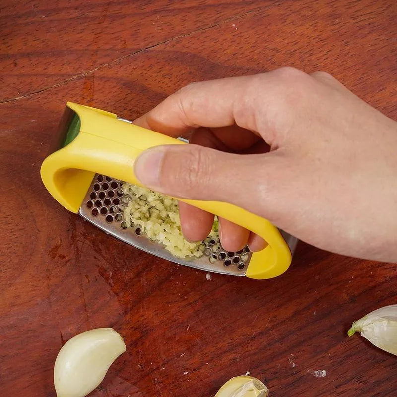 Stainless steel garlic press with coloured ergonomic handle on a kitchen counter.