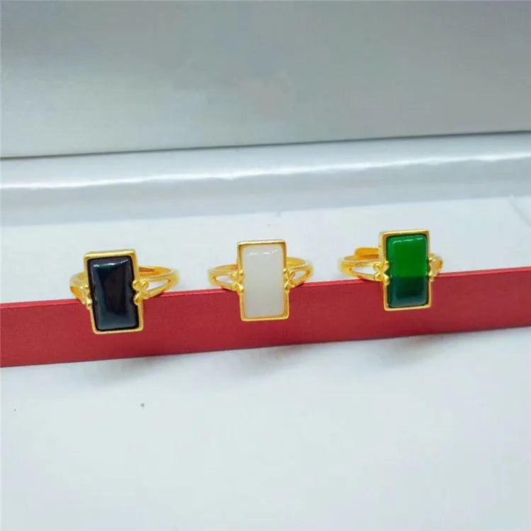 Adjustable gold-plated brass ring with a coloured gemstone inlay on a plain background.
