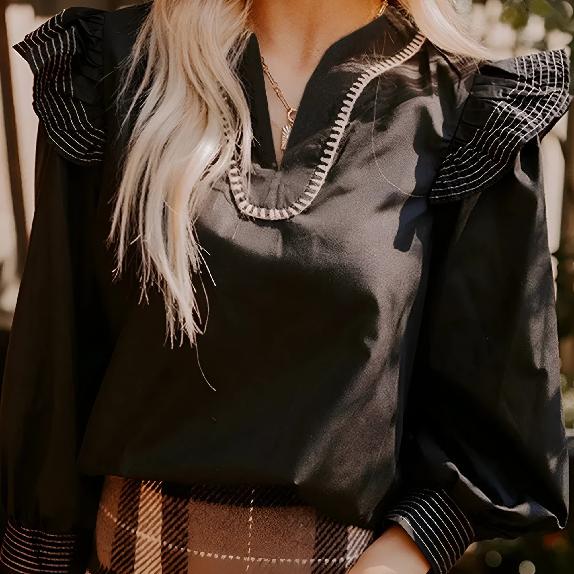Black women's V-neck blouse with contrast stitching and long ruffle sleeves on a hanger.