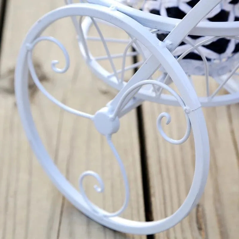 Black wrought iron tricycle plant stand with three round basket tiers and decorative scroll wheels