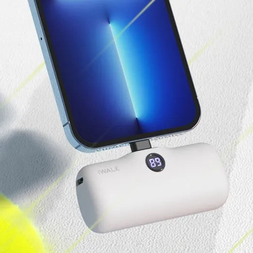 Compact cylindrical white power bank with digital battery percentage screen on a wooden table