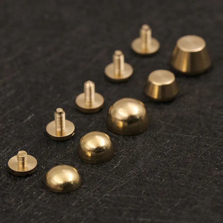 Brass decorative buckle with set of round and bucket-shaped brass foot nails on a surface.
