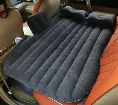Black inflatable car bed with flocked surface and two pillows, folded next to its storage bag.