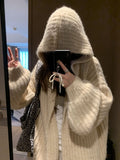 A woman wearing a loose-fit dark grey hooded cardigan made from thick acrylic blend fabric.