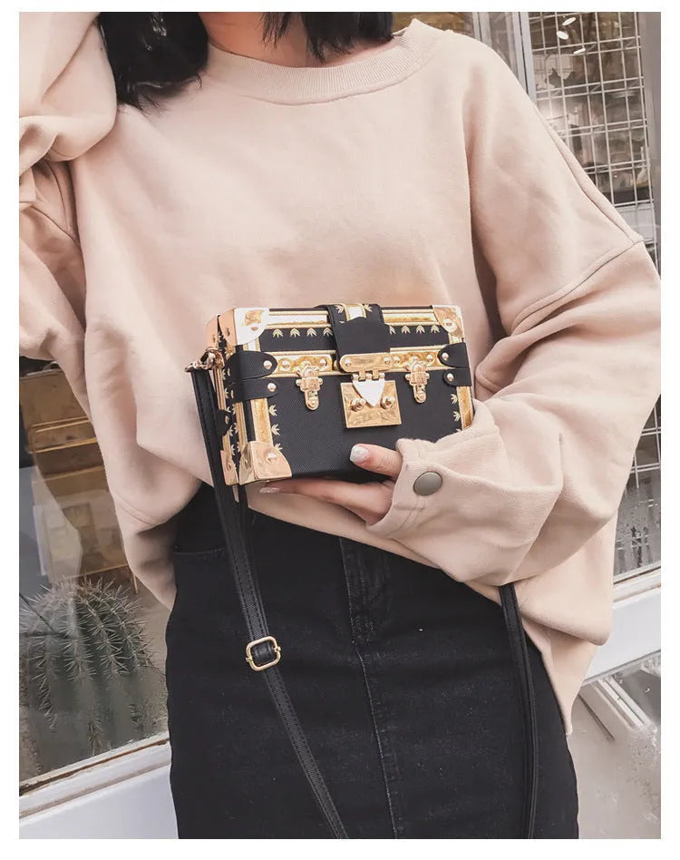 Hard-sided black women's shoulder bag with a flap closure, adjustable strap, and decorative metal rivets.