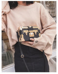 Hard-sided black women's shoulder bag with a flap closure, adjustable strap, and decorative metal rivets.