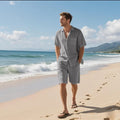 A man wearing a light blue linen-blend short sleeve shirt and matching shorts on a beach.