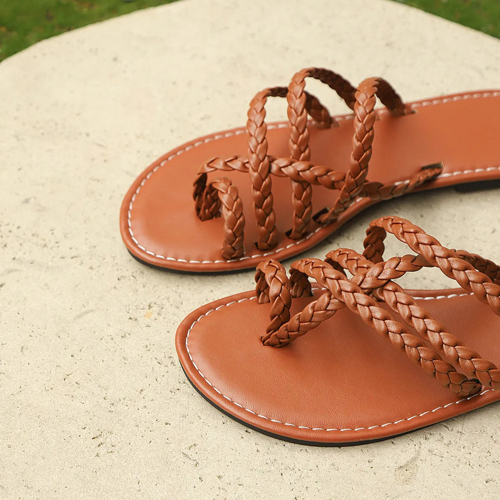 Women's white woven flat sandals with an adjustable clip-toe strap on a wooden deck.