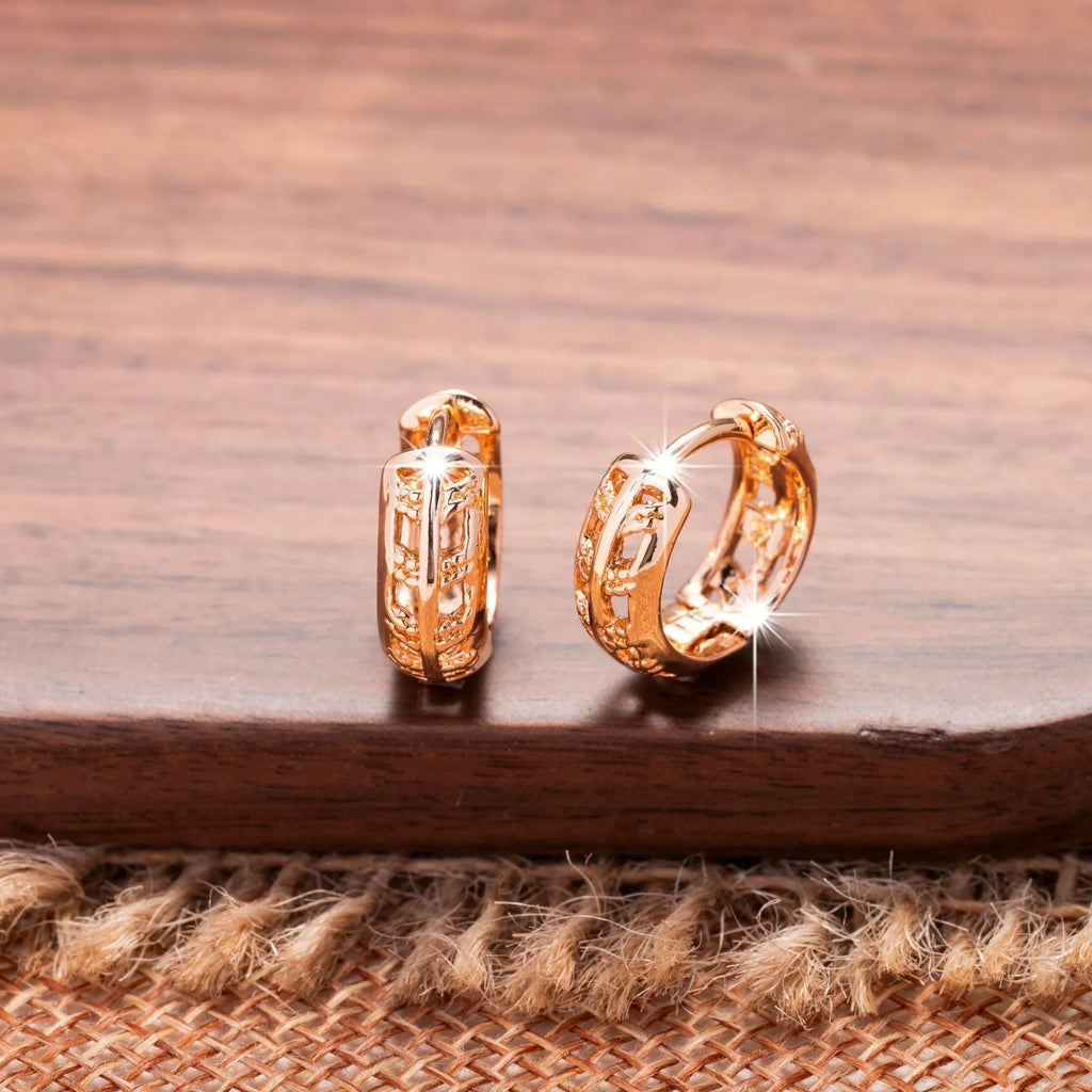 Close-up of rose gold plated copper stud earrings with hollow leaf and heart shapes on a grey background.